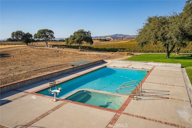 view of swimming pool featuring a patio area, a mountain view, a rural view, and a diving board