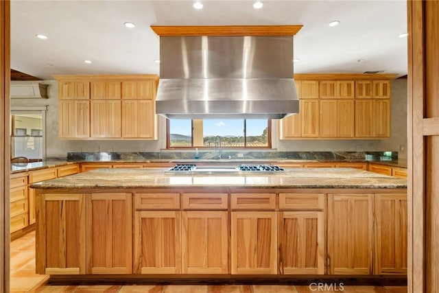 kitchen featuring a center island, light stone counters, stainless steel gas stovetop, and wall chimney exhaust hood