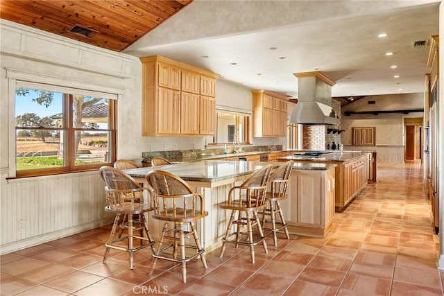 kitchen with a kitchen breakfast bar, light brown cabinetry, light stone counters, kitchen peninsula, and island exhaust hood