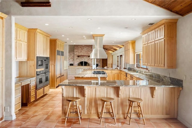 kitchen featuring kitchen peninsula, light brown cabinetry, a breakfast bar, stainless steel double oven, and sink