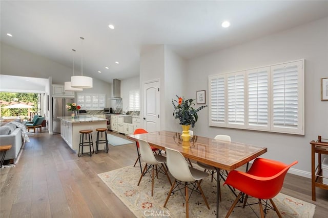 dining room with light wood-type flooring and high vaulted ceiling