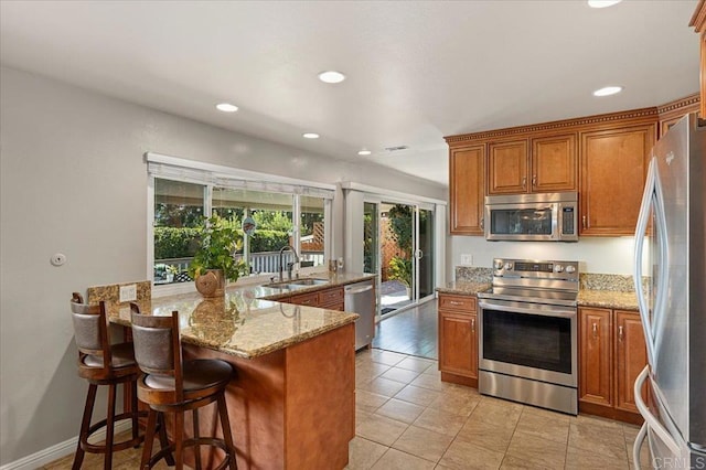 kitchen featuring light stone countertops, sink, kitchen peninsula, a kitchen bar, and appliances with stainless steel finishes