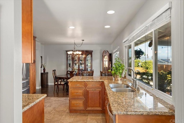 kitchen featuring light stone counters, sink, decorative light fixtures, and kitchen peninsula