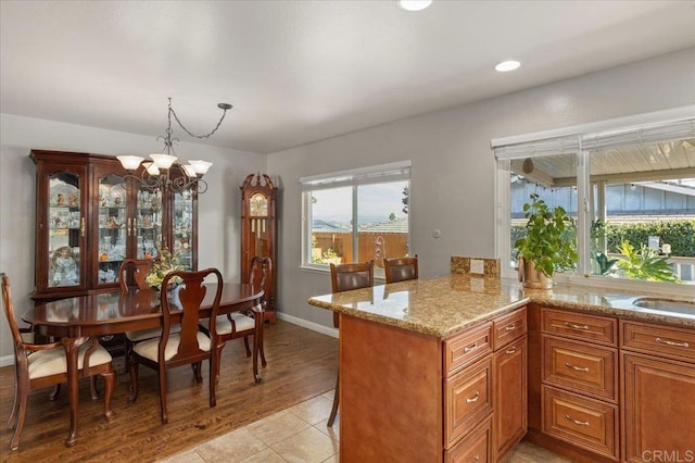 kitchen with a notable chandelier, light stone countertops, kitchen peninsula, pendant lighting, and light tile patterned flooring