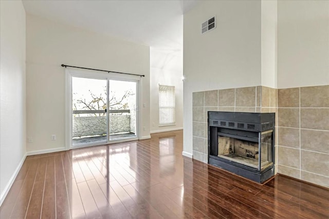 unfurnished living room with a tiled fireplace, hardwood / wood-style floors, and a high ceiling