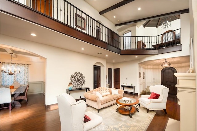 living room featuring a chandelier, a high ceiling, hardwood / wood-style flooring, and beam ceiling