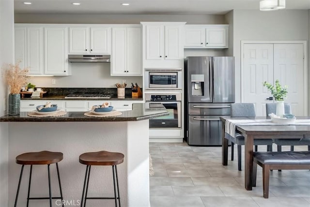 kitchen with a breakfast bar, white cabinets, light tile patterned floors, and appliances with stainless steel finishes