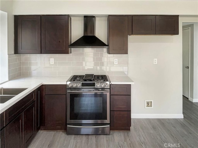 kitchen with light hardwood / wood-style floors, gas stove, tasteful backsplash, dark brown cabinets, and wall chimney exhaust hood