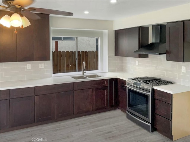 kitchen featuring tasteful backsplash, sink, stainless steel range with gas cooktop, dark brown cabinetry, and wall chimney exhaust hood