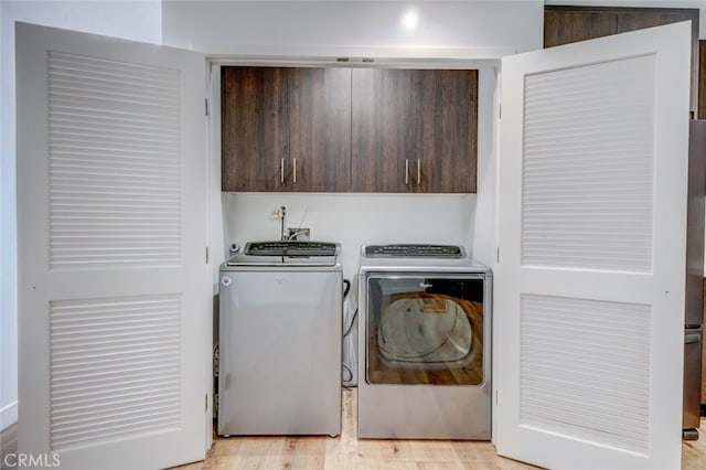 laundry area with cabinets, washer and dryer, and light hardwood / wood-style floors