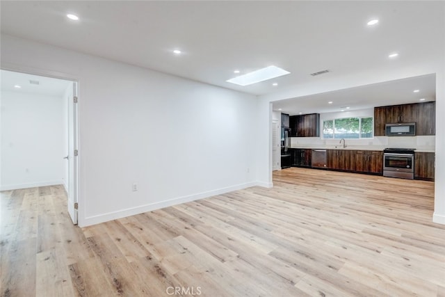 unfurnished living room featuring a skylight, light hardwood / wood-style flooring, and sink