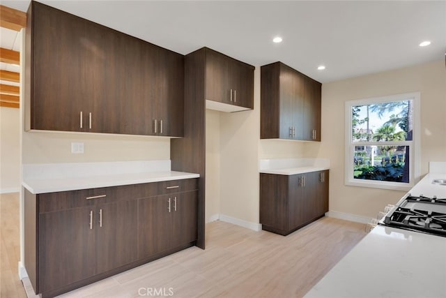 kitchen with white gas stove, dark brown cabinets, and light wood-type flooring