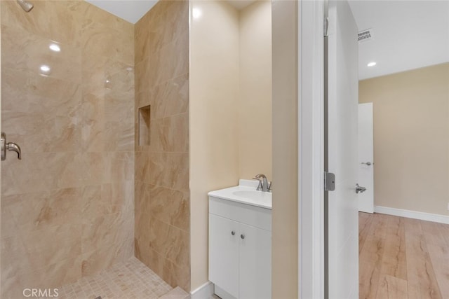 bathroom with hardwood / wood-style flooring, vanity, and tiled shower