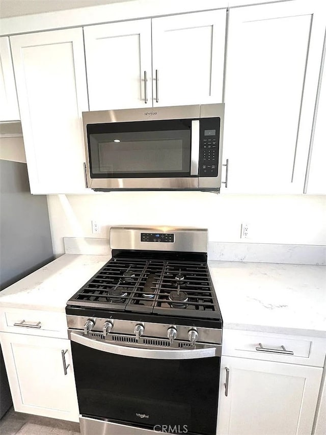 kitchen featuring light stone countertops, stainless steel appliances, and white cabinetry