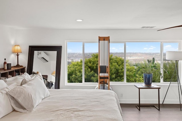 bedroom featuring a wall mounted AC, multiple windows, and hardwood / wood-style flooring