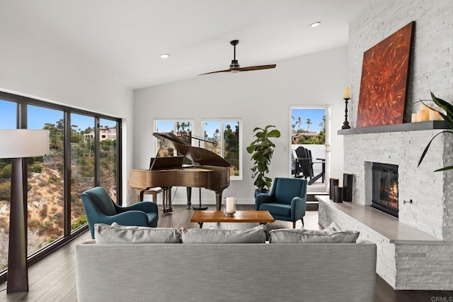 living room with ceiling fan, lofted ceiling, a stone fireplace, and light wood-type flooring