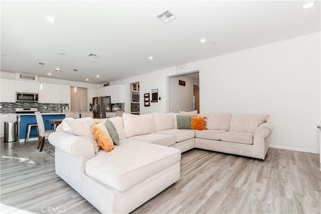 living room with recessed lighting, visible vents, baseboards, and light wood-style flooring