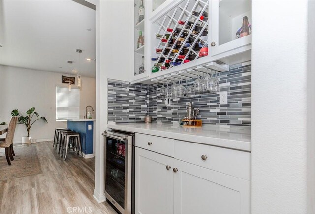 bar featuring tasteful backsplash, wine cooler, light wood finished floors, a dry bar, and hanging light fixtures