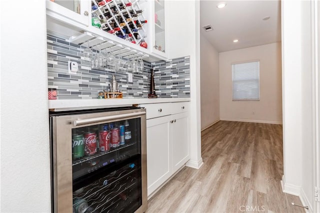 bar featuring beverage cooler, visible vents, light wood finished floors, indoor wet bar, and decorative backsplash