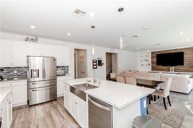 kitchen featuring a center island with sink, appliances with stainless steel finishes, hanging light fixtures, white cabinets, and sink