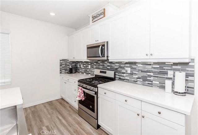 kitchen with light wood finished floors, light countertops, appliances with stainless steel finishes, white cabinetry, and backsplash