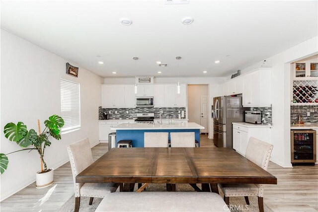 dining space featuring indoor bar, wine cooler, light wood-style floors, and recessed lighting