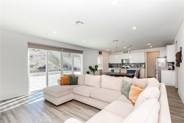 living area with recessed lighting, visible vents, light wood-style flooring, and baseboards