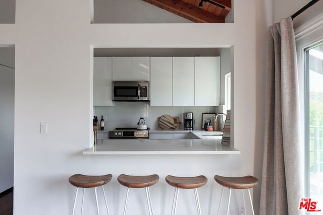 kitchen with sink, stainless steel appliances, white cabinets, decorative backsplash, and kitchen peninsula