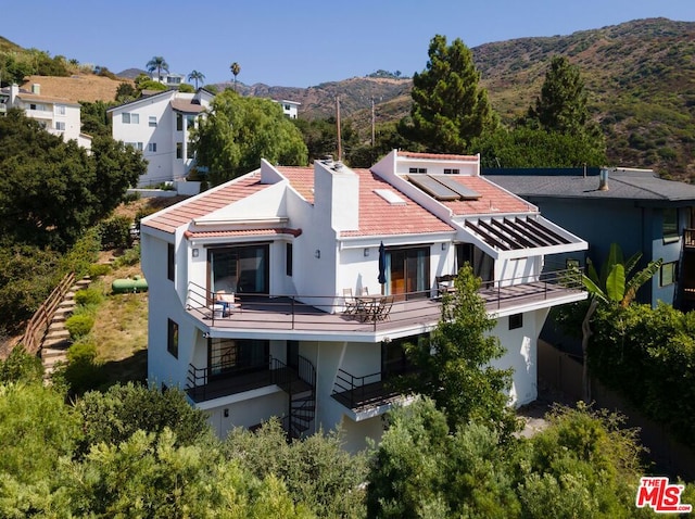 rear view of house with a mountain view, a balcony, and solar panels