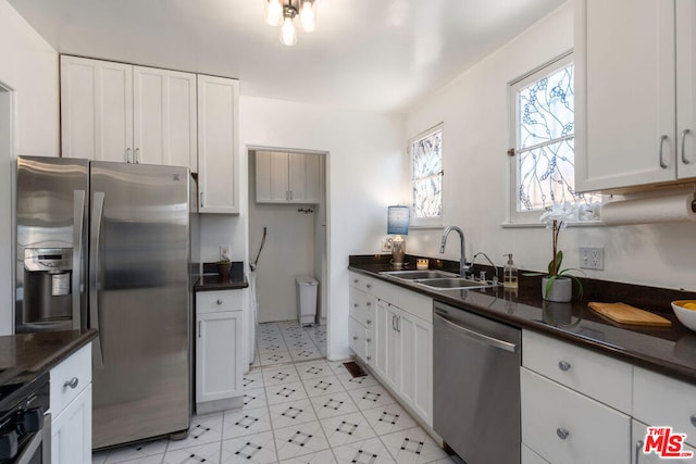 kitchen with white cabinets, stainless steel appliances, dark stone countertops, and sink