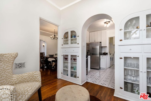 interior space featuring wood-type flooring, white cabinetry, a chandelier, washing machine and dryer, and stainless steel fridge