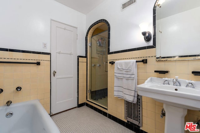 bathroom with a tub to relax in, tile walls, sink, and tile patterned flooring