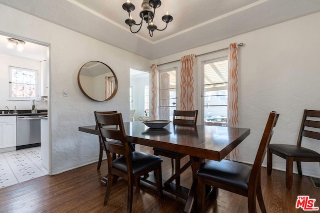 dining area featuring sink, a chandelier, a raised ceiling, and hardwood / wood-style floors