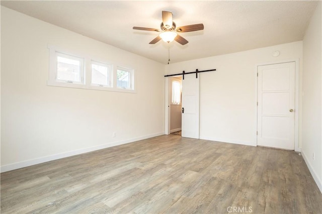 empty room featuring a barn door, light hardwood / wood-style flooring, and ceiling fan