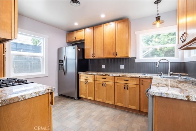 kitchen featuring sink, hanging light fixtures, stainless steel appliances, light stone counters, and backsplash