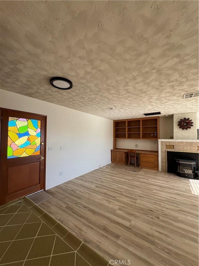 unfurnished living room with a textured ceiling, built in desk, dark wood finished floors, and visible vents