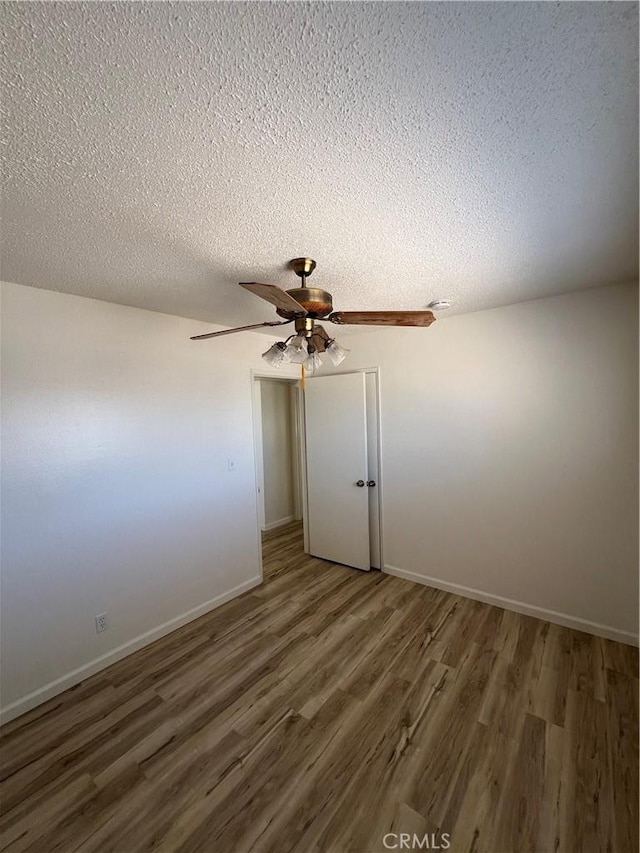 spare room with dark wood-style flooring, ceiling fan, a textured ceiling, and baseboards