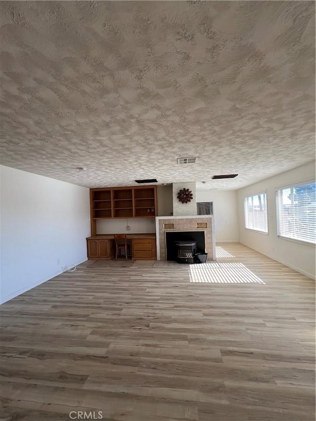 unfurnished living room with a textured ceiling, visible vents, and wood finished floors