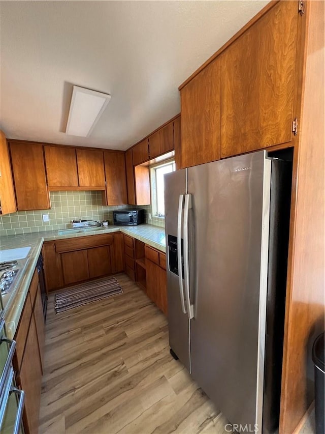 kitchen featuring light wood-style flooring, stainless steel fridge with ice dispenser, light countertops, backsplash, and brown cabinets