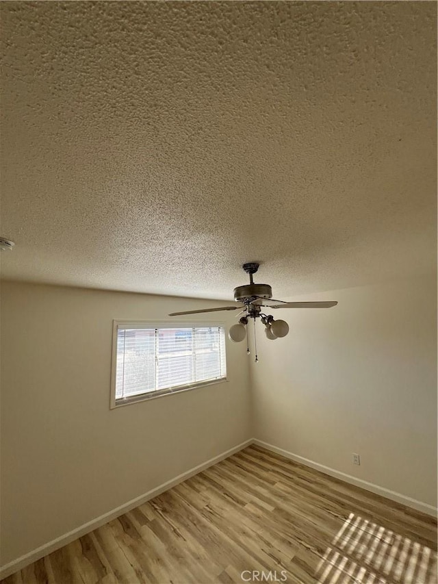 spare room with a textured ceiling, ceiling fan, wood finished floors, and baseboards