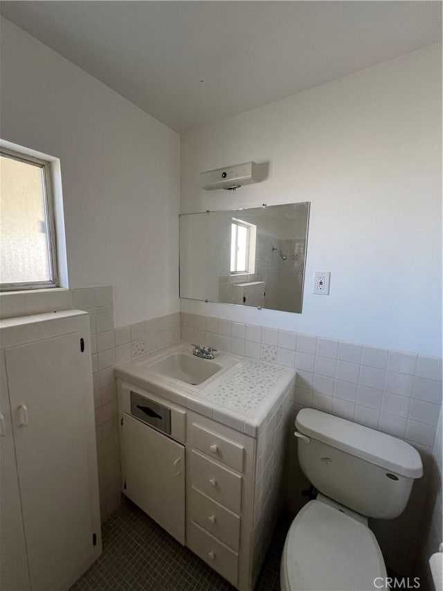 half bathroom featuring tile patterned flooring, toilet, vanity, tile walls, and wainscoting