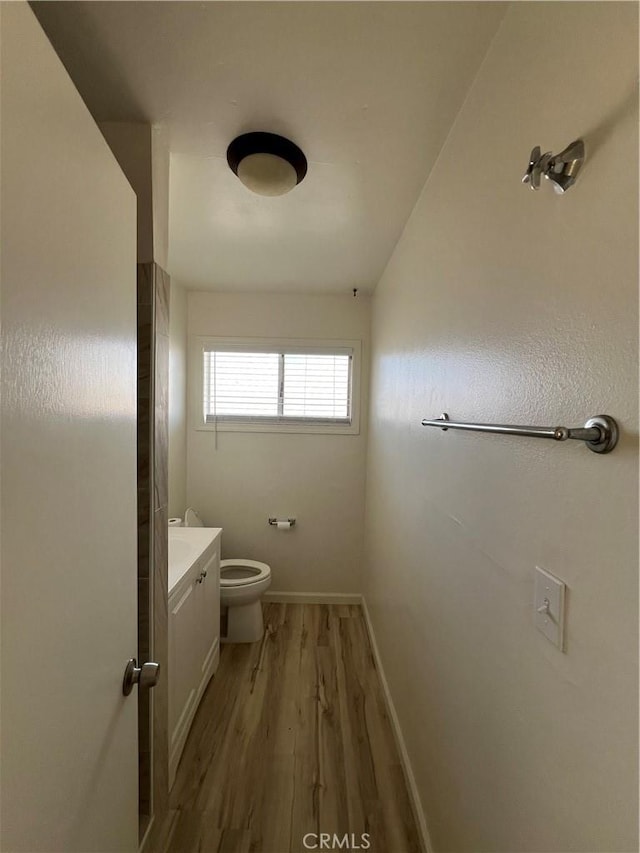 bathroom featuring toilet, baseboards, wood finished floors, and vanity