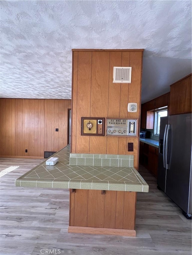 kitchen featuring tile countertops, a textured ceiling, stainless steel fridge, and visible vents