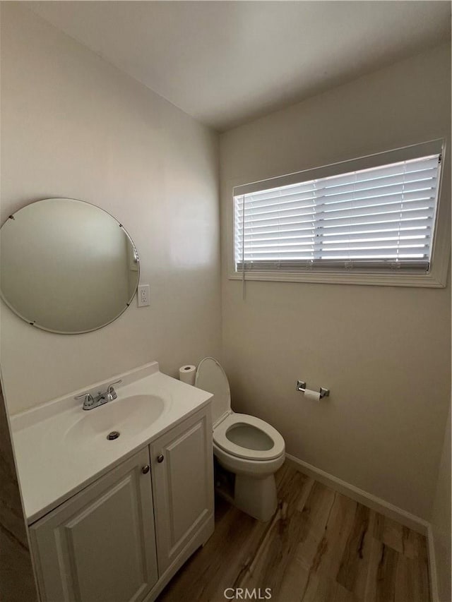 half bath featuring toilet, baseboards, wood finished floors, and vanity