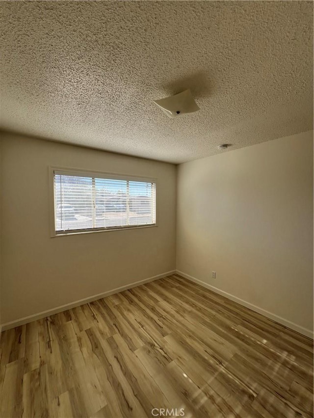 empty room with a textured ceiling, wood finished floors, a wealth of natural light, and baseboards