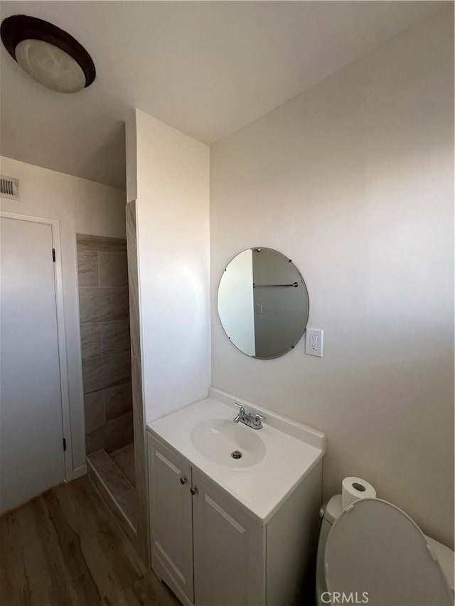 bathroom with visible vents, toilet, a stall shower, vanity, and wood finished floors