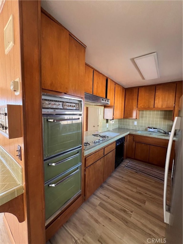 kitchen featuring wall oven, black dishwasher, tasteful backsplash, light countertops, and under cabinet range hood