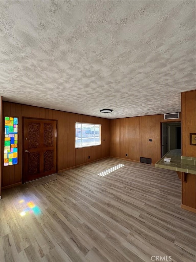 unfurnished living room with light wood-type flooring, visible vents, a textured ceiling, and baseboards