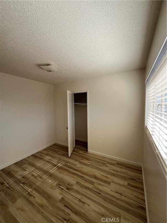 unfurnished bedroom with dark wood-style floors, a closet, a textured ceiling, and baseboards