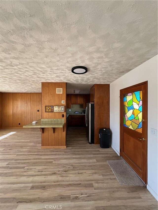 interior space featuring tile countertops, a breakfast bar, visible vents, freestanding refrigerator, and brown cabinetry